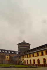 Fototapeta premium A rainy view of a castle watch tower with clouds and yellow buildings