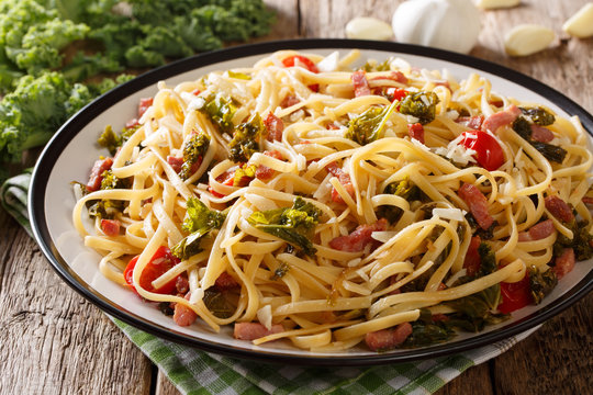 Delicious spicy linguine pasta with fried cabbage kale, bacon, tomatoes, garlic and parmesan close-up on a plate. horizontal