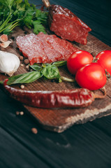 Smoked salami on a black table and a brown board. Sausages with rosemary, garlic and pepper and tomato cherry, dill, parsley
