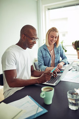 Two smiling office colleagues using a laptop and talking togethe
