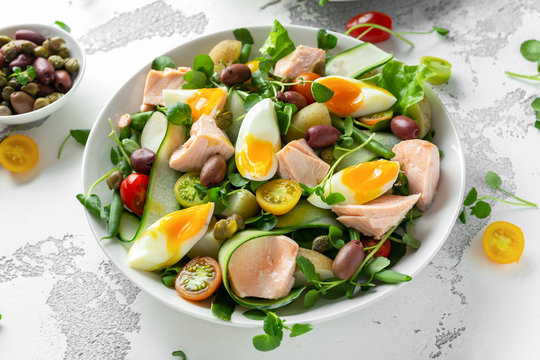 Healthy Nicoise salad with salmon, colourful sweet cherry tomatoes, olives, green beans, cucumber ribbons, soft boiled eggs, water-cress leaves with Mediterranean seasoning