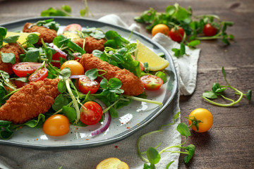 Fresh salad with chicken nuggets, cherry tomatoes and green vegetables in a rustic wooden table