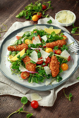 Fresh salad with chicken nuggets, cherry tomatoes, goat cheese and green vegetables in a rustic wooden table