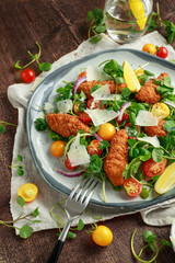 Fresh salad with chicken nuggets, cherry tomatoes, goat cheese and green vegetables in a rustic wooden table