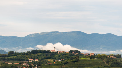 Village of Steverjan, San Floriano del Collio, Italy with church in front of white low white cloud, Goriska Brda, with vineyards and orchards