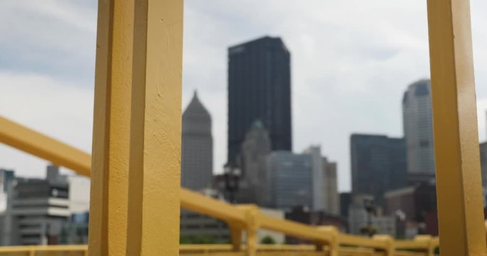 A daytime tracking dolly shot of the Pittsburgh skyline as seen through the yellow steel beams of the Andy Warhol Bridge.  	