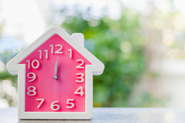 Pink clock with home shape at 12 o'clock against blurred natural green background for family time concept