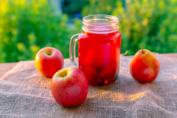 jar full of fruit juice with red apples on nature background