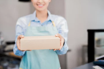 Tuinposter Mid section portrait of unrecognizable woman wearing apron holding box with takeaway food and smiling happily, copy space © Seventyfour