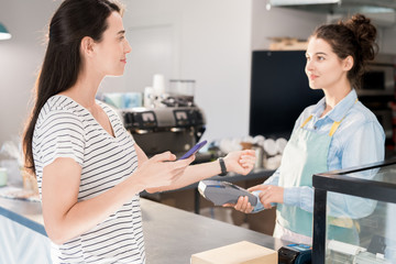 Waist up portrait of young woman paying via smart watch  and smartphone in local shop, copy space