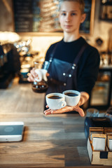 Young male barista holds two cups of fresh coffee