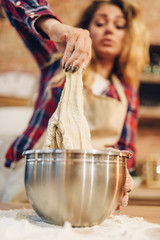 Housewife in an apron cooking dough in metal bowl