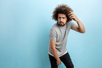 A curly-headed handsome man wearing a gray T-shirt is standing, leaning forwards, with a serious...