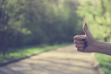 Girl making a thumbs up (like) gesture against sunny green background. Concept of hitchhiking, traveling, youth. Vintage colors