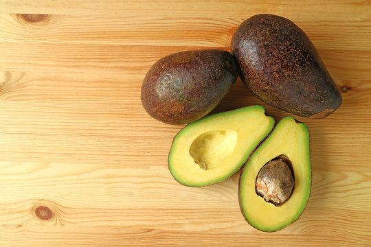 Top View of Ripe Avocados Both Whole Fruits and Cut In Half Isolated on Wooden Background 