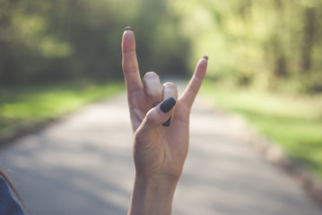 Girl making a sign of the horns gesture (satan's fingers) against sunny green background.