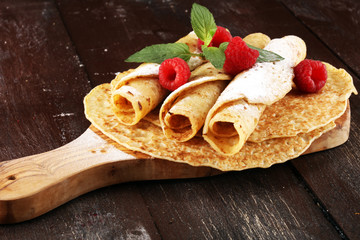 Homemade crepes served with fresh raspberrries and powdered sugar on rustic table.