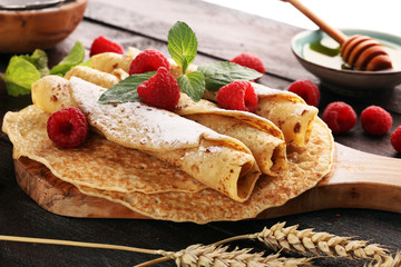 Homemade crepes served with fresh raspberrries and powdered sugar on rustic table.
