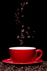 Coffee beans falling into red coffee cup.