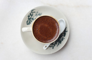White coffee served in cup with saucer on white marble table