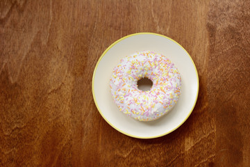 donut with glaze on a saucer and on a wooden table-top