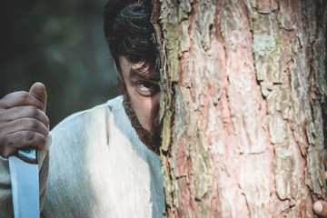 maniac with a knife stands behind a tree