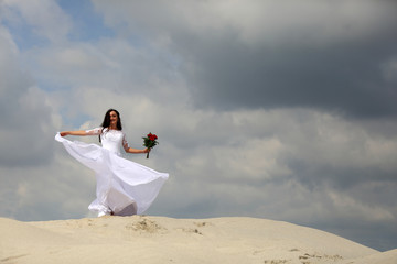 Ślub, wesele, piękna dziewczyna w białej sukni tańczy na szzycie piaszczystej wydmy. - obrazy, fototapety, plakaty