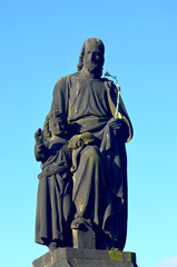 Fototapeta premium A weathered statue of St. Jospeh and Jesus is on the Charles Bridge, Prague. St Jospeh hold a flowering rod in one hand. Behind is a bright blue sky.
