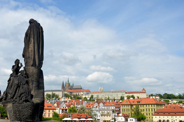 A statue looks from the Charles Bridge towards Prague Castle. Storm clouds are gathering in the...