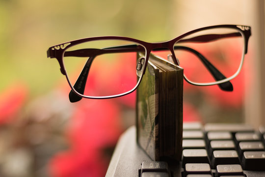 Glasses, a book and a computer are on a blurred background of nature. Workplace by a window.