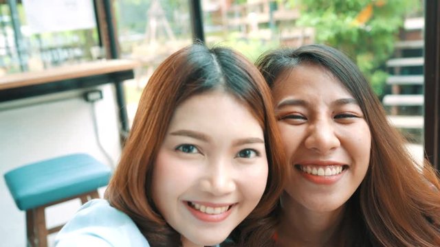 Beautiful happy Asian women lesbian lgbt couple sitting each side eating a plate of Italian seafood spaghetti and french Fries at restaurant or cafe. Female couple using smartphone for selfie.