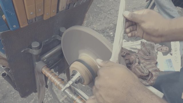 seller sharpening knife using grinder in streets near KR market, India in slow motion