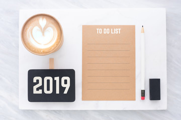 2019 to do list on brown recycle paper with pencil,clip blackboard,pencil,eraser and coffee cup on white and grey marble table.mock up for adding text,new year resolution concept.