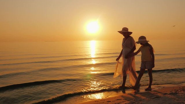 Summer vacation with a child - a woman with her daughter strolling along the seashore at sunset
