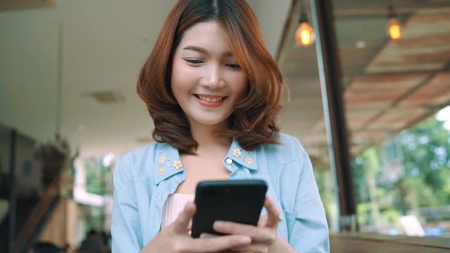 Cheerful happy asian young woman sitting in cafe using smartphone for talking, reading and texting. Women lifestyle concept.