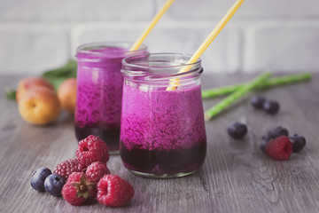 Homemade smoothies of fresh berries and fruits in glasses on gray wooden table.