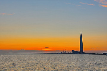 The Lahta center skyscraper buidling on the shore of Finish bay near Petersburg city in the mouth of Neva river in the rays of setting sun. The beautiful orange and red urban landscape 