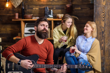 Man with stylish beard enjoying creative process. Musician entertaining his wife and daughter. Girls with smiling face listening to music, happiness concept. Bearded man in red sweater playing guitar