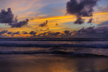 Fototapeta na wymiar Silhouettes of a wave and clouds on a color sky during sunset. Evening on a tropical beach.