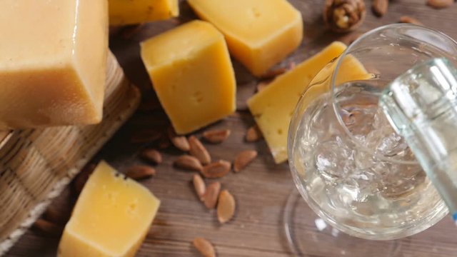Wine and cheese. Food art. Different sorts of hard cheese beautifully surved on a wooden background. White wine is being poured into wine glass.