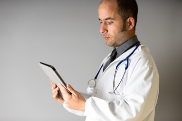 A doctor with a stethoscope around his neck looks at a tablet