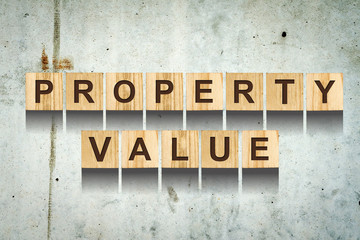 Property value, inscription made of wooden cubes on of a concrete wall.