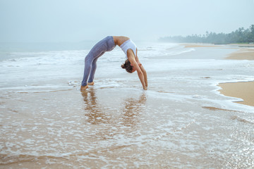 Caucasian woman practicing yoga at seashore of tropic ocean