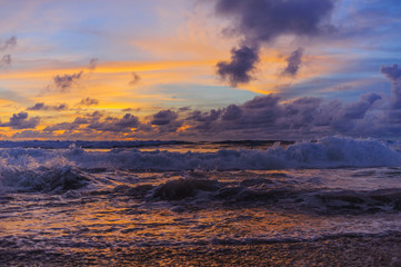 Waves and splashes on the sandy beach of the tropical island. Beautiful romantic colors sunset by the sea.