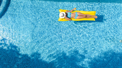 Beautiful young girl relaxing in swimming pool, swims on inflatable mattress and has fun in water on family vacation, tropical holiday resort, aerial top view from above

