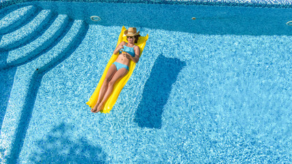 Beautiful young girl relaxing in swimming pool, swims on inflatable mattress and has fun in water on family vacation, tropical holiday resort, aerial top view from above
