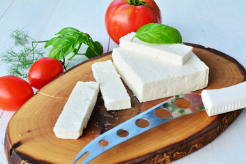 Goat cheese on wooden board with tomatoes and herbs closeup