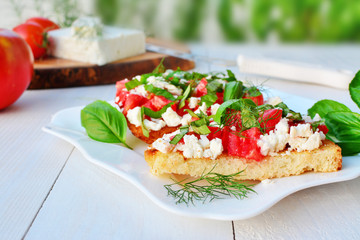 Tomato bruschettas with goat cheese and basil on plate over white wooden table