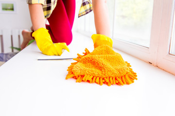 Woman in protective gloves is smiling and wiping dust using a spray and a duster