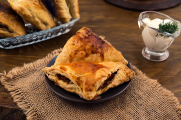 Baked puff with Apple filling, mayonnaise with dill in a gravy boat, napkin of rough fabric, all on a wooden background.